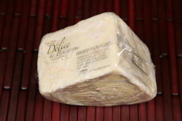 A wedge of Le Délice de Bourgogne triple-cream cheese with its bloomy rind